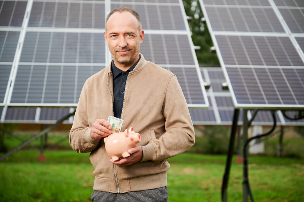 Investing in alternative energy innovations. Professional investor making investment in ecological resources. Young male in casual clothes holding piggy bank and smiling to camera.